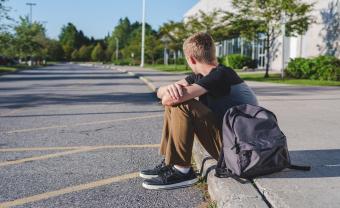 Image of a young white male student sitting alone on sidewalk