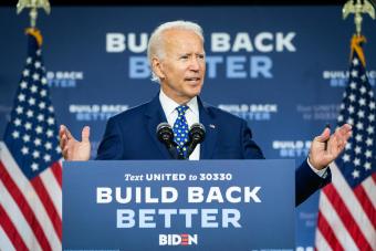 President Biden standing at a podium reading "Build Back Better" with a "Build Back Better" backdrop behind him