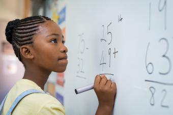 [image of a young student standing at the dry erase board doing a math problem]