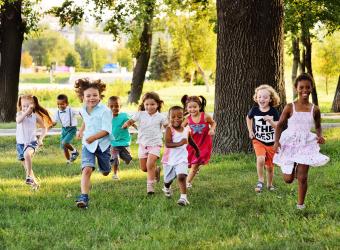 Preschool age children running on the grass away from trees.